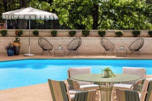 Een zwembadterras met een ronde tafel, stoelen, een witte parasol en potplanten.
