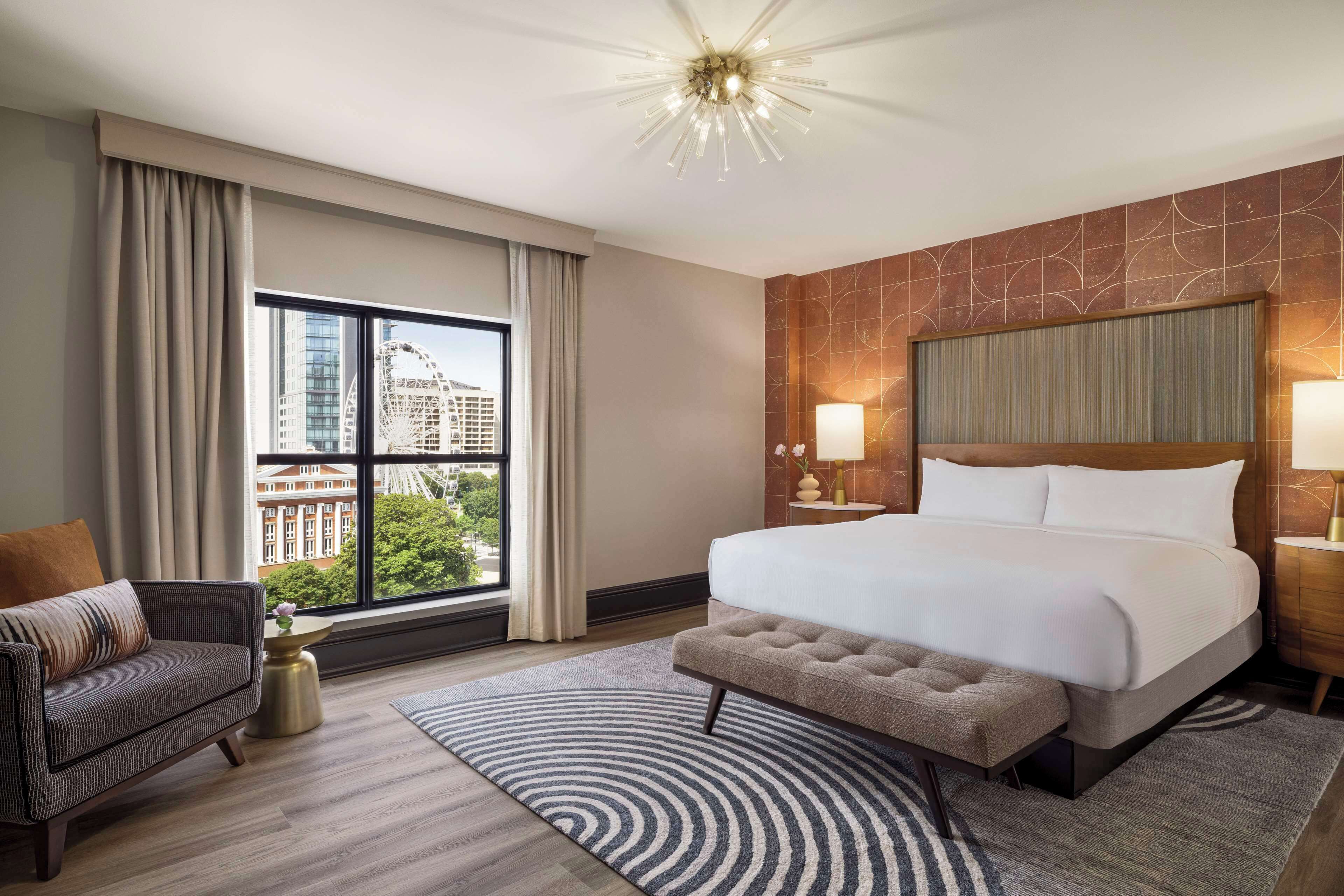 Une chambre d’hôtel avec un grand lit, un canapé, une table de chevet et une vue sur le paysage urbain par la fenêtre.
