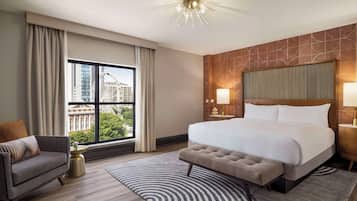 Une chambre d’hôtel avec un grand lit, un canapé, une table de chevet et une vue sur le paysage urbain par la fenêtre.