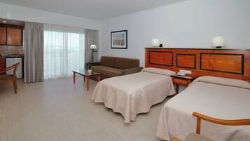 Habitació d'hotel amb dos llits, un sofà, escriptori, làmpada i vistes a la ciutat.