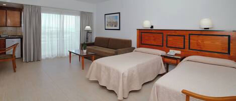 A hotel room with two beds, a sofa, a desk, a lamp, and a view of the city.