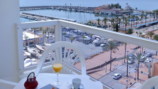 A balcony with a table set for breakfast, overlooking a marina and beach.
