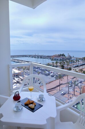 Un balcón con una mesa lista para el desayuno, con vista a un puerto deportivo y una playa.