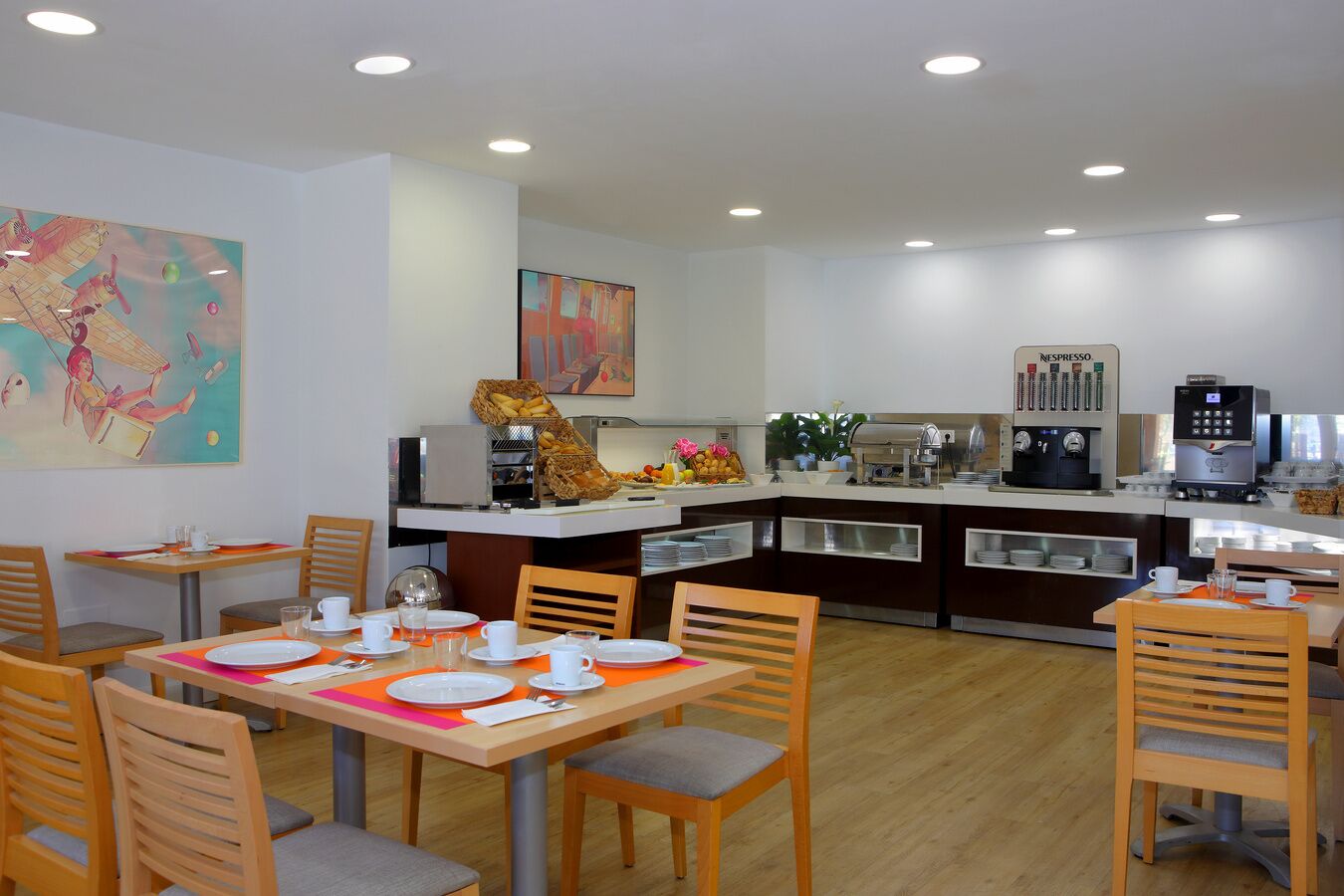 Un espace repas moderne avec des tables et des chaises en bois, un buffet proposant des plats et des boissons, et une machine à café.