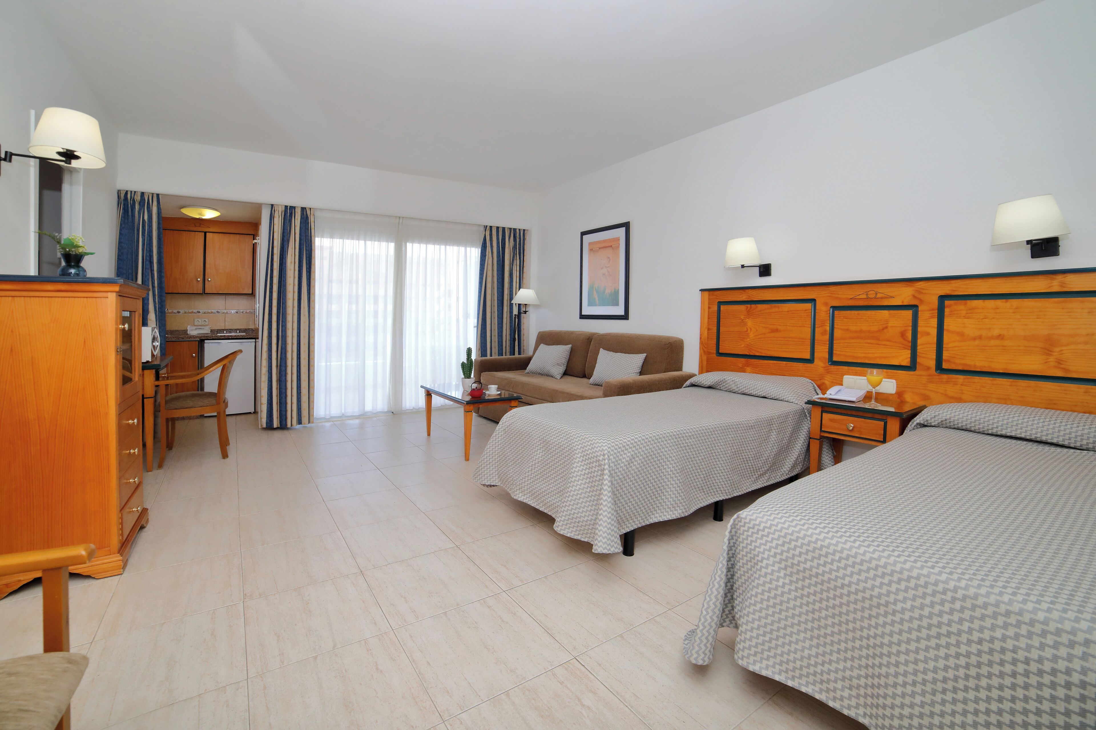 Habitación de hotel con dos camas, un sofá, un escritorio y una kitchenette.