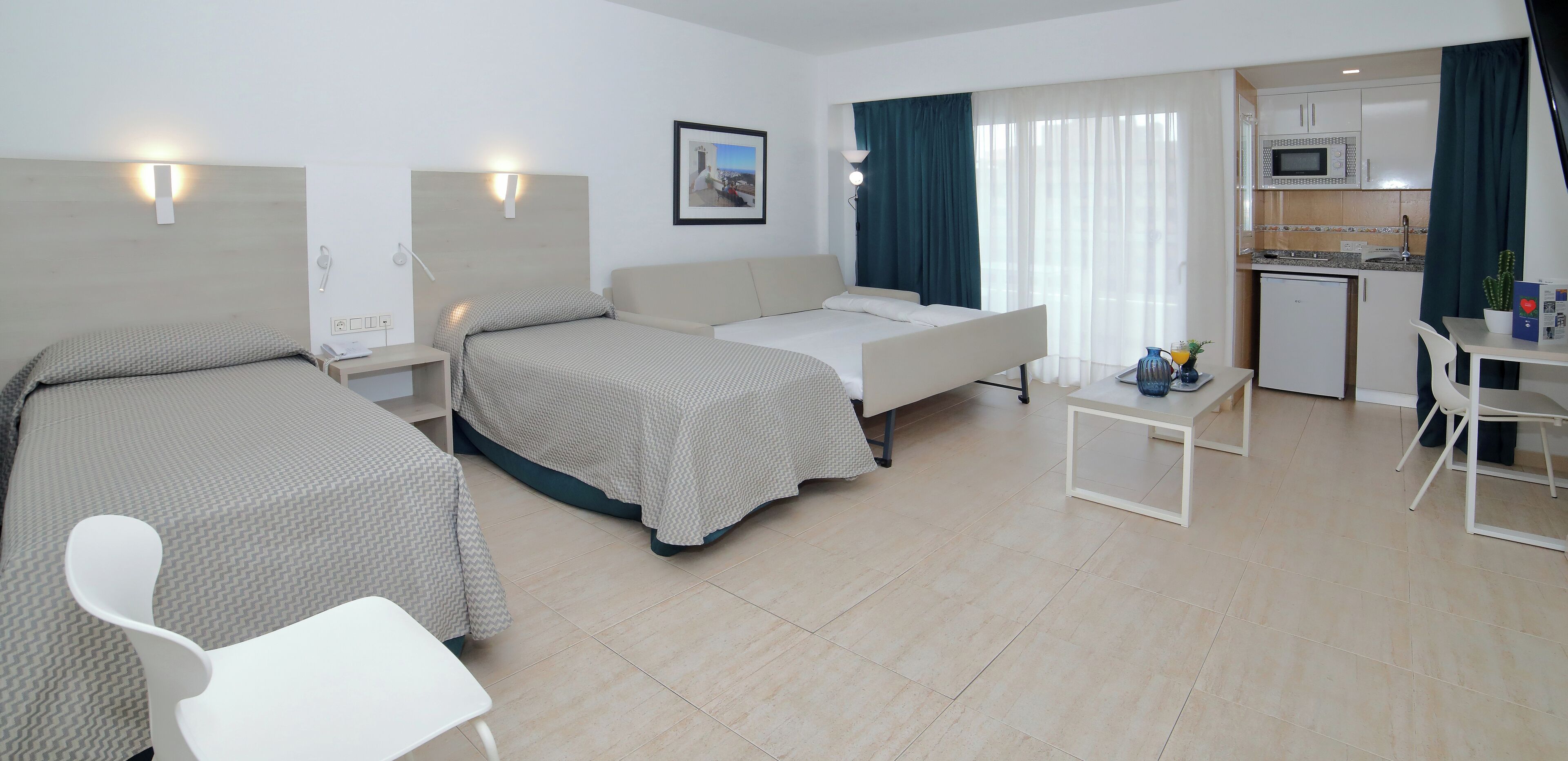 Habitación de hotel con dos camas, un sofá, una pequeña mesa de comedor y una kitchenette.
