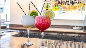 Three cocktails with straws and fruit garnishes on a bar counter.