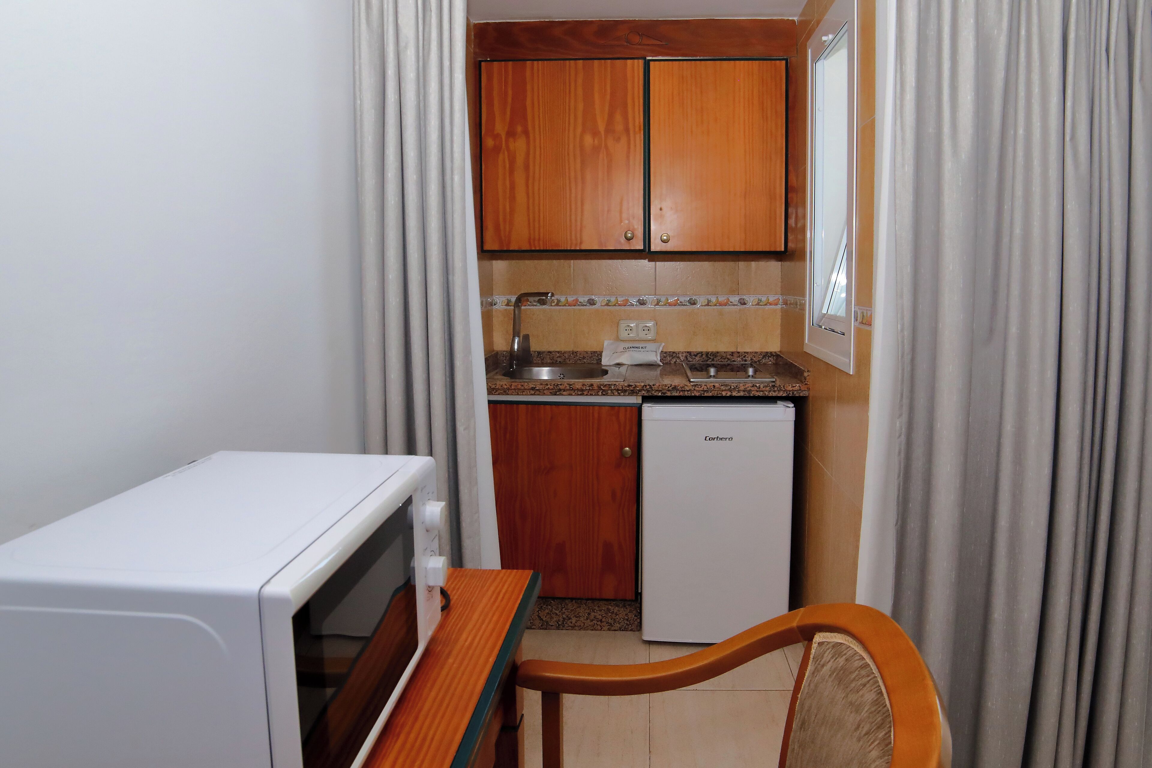 Una kitchenette compacta con armarios de madera, un microondas, un refrigerador y una pequeña mesa de comedor.