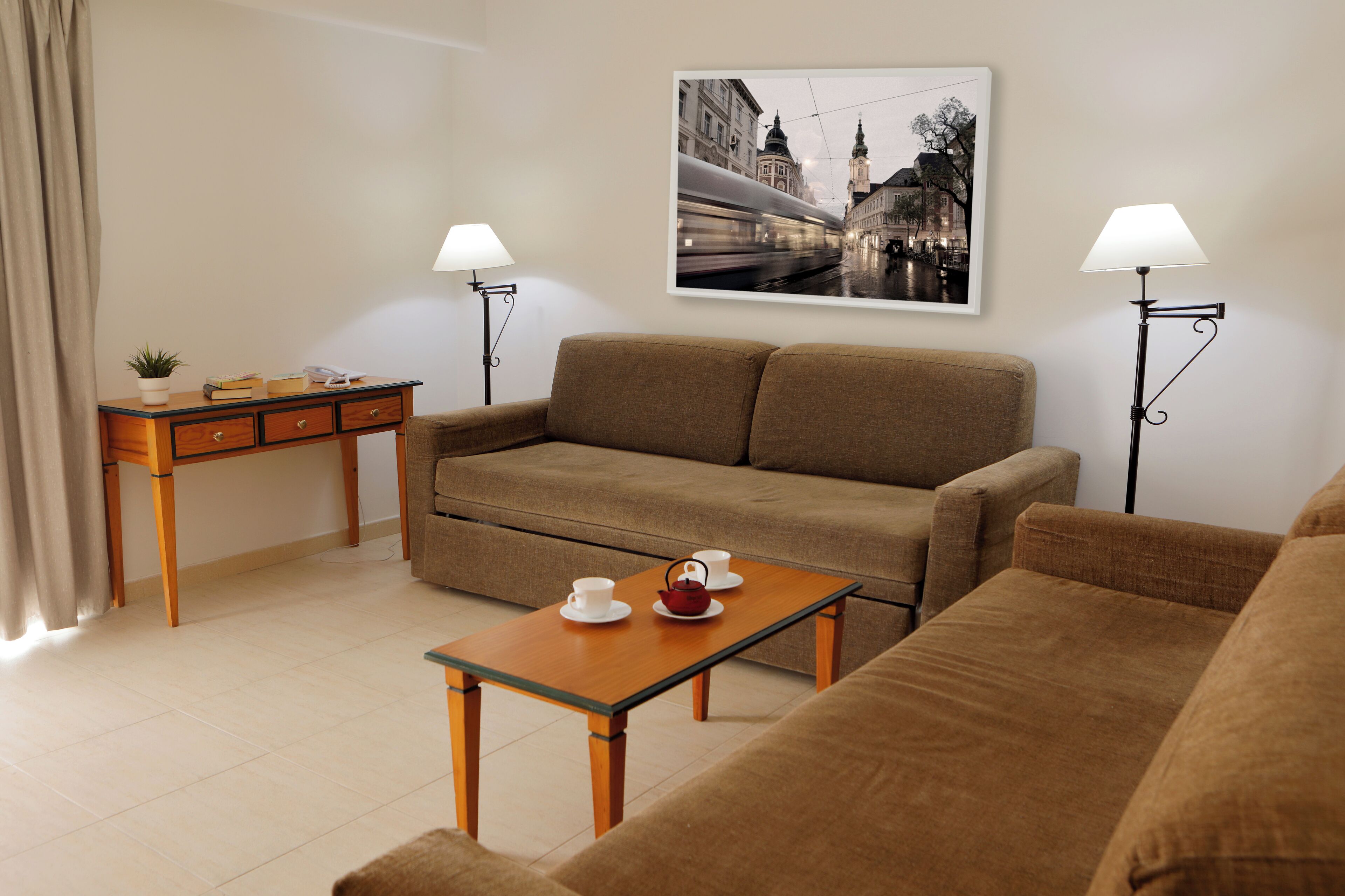 A modern living room with a sofa, a coffee table with cups and a teapot, a side table with books and a plant, and two floor lamps.