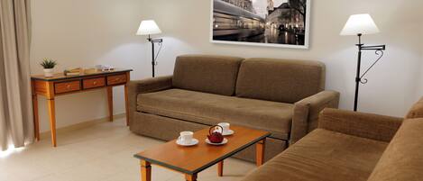 A modern living room with a sofa, a coffee table with cups and a teapot, a side table with books and a plant, and two floor lamps.