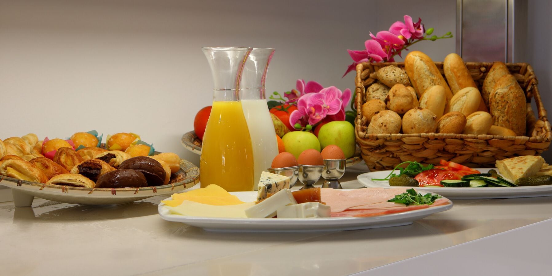 A breakfast buffet with various pastries, cheeses, fruits, and bread.