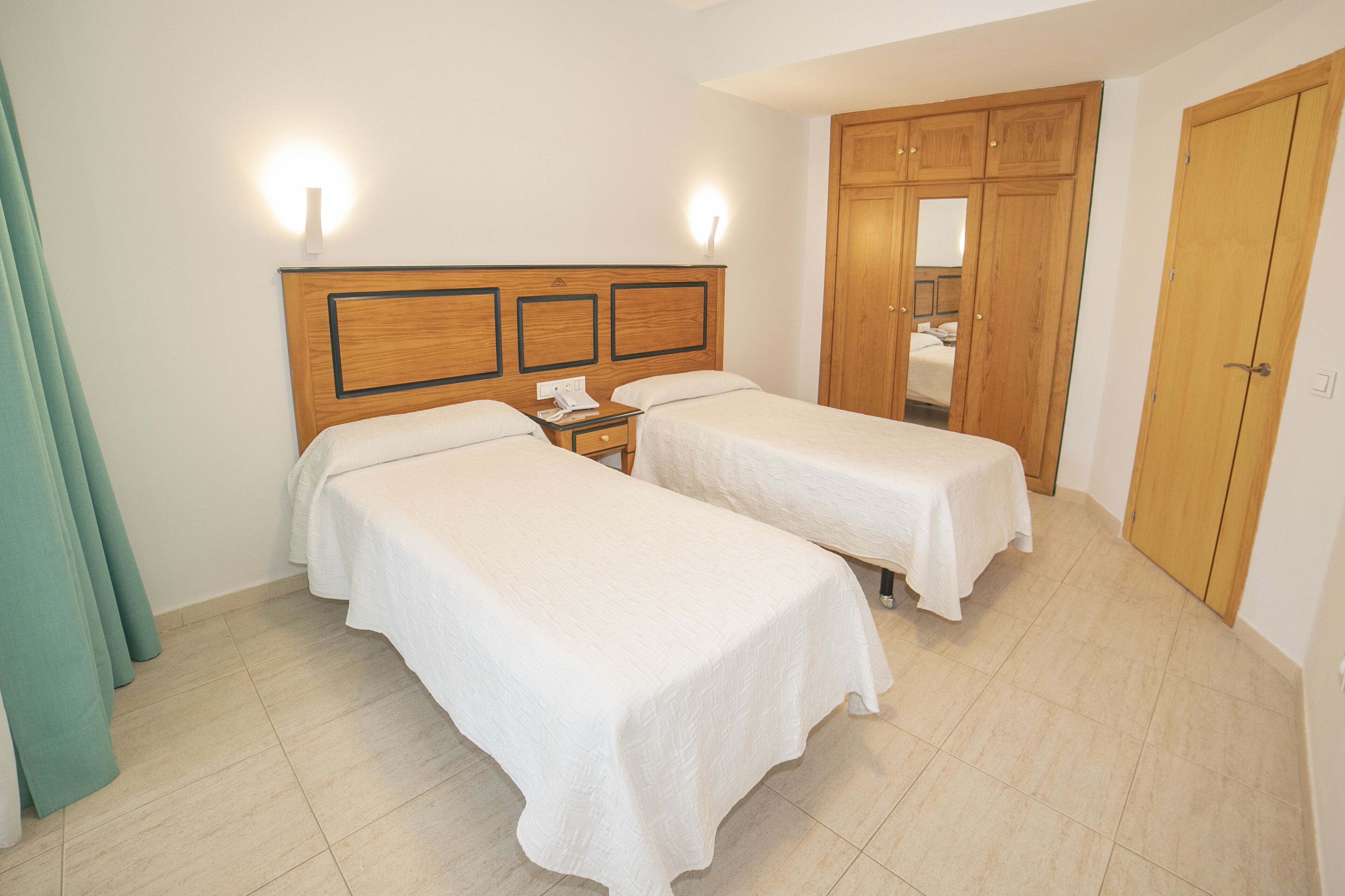 Habitación de hotel con dos camas individuales, un armario de madera y un baño visible a través de una puerta.