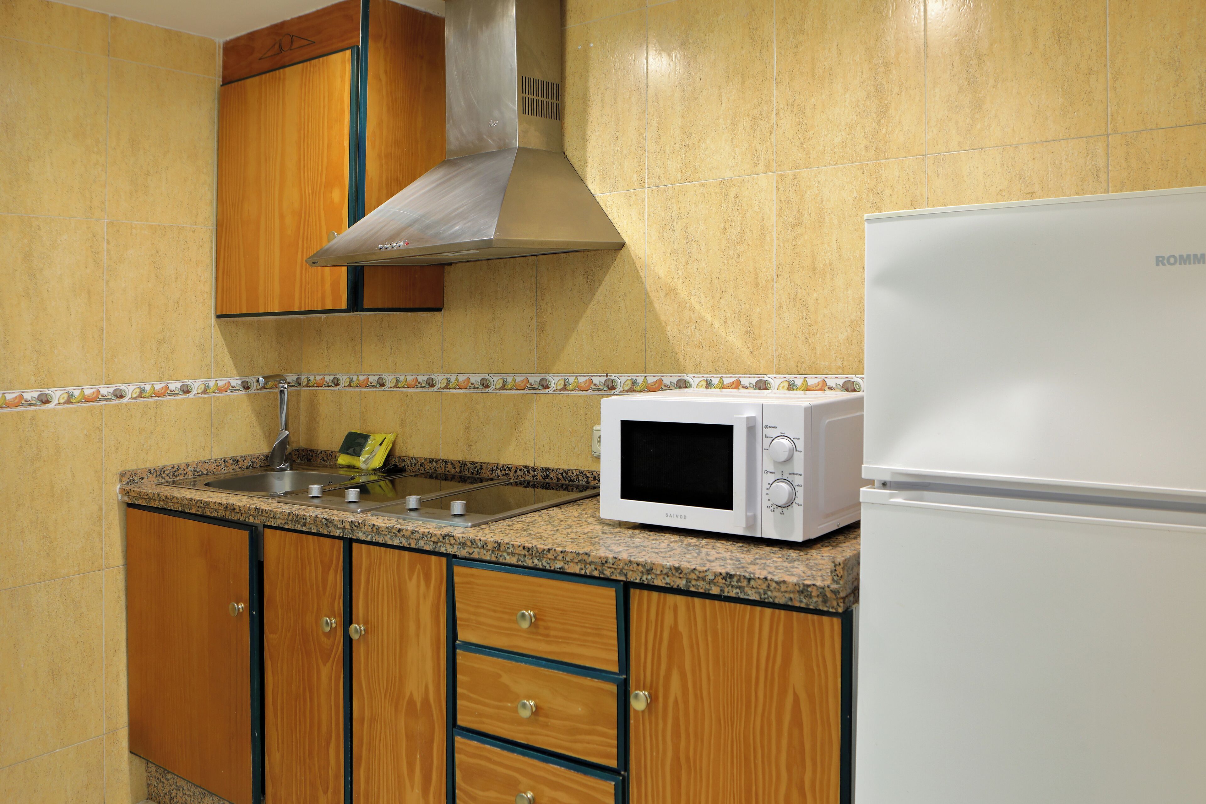 Una cocina con armarios de madera, una campana extractora de acero inoxidable, un microondas y un refrigerador blanco.
