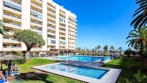 A hotel with multiple balconies, a swimming pool, and palm trees.