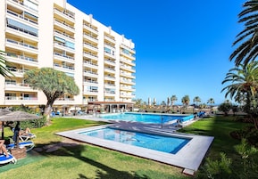Una piscina al aire libre, sombrillas, sillones reclinables de piscina