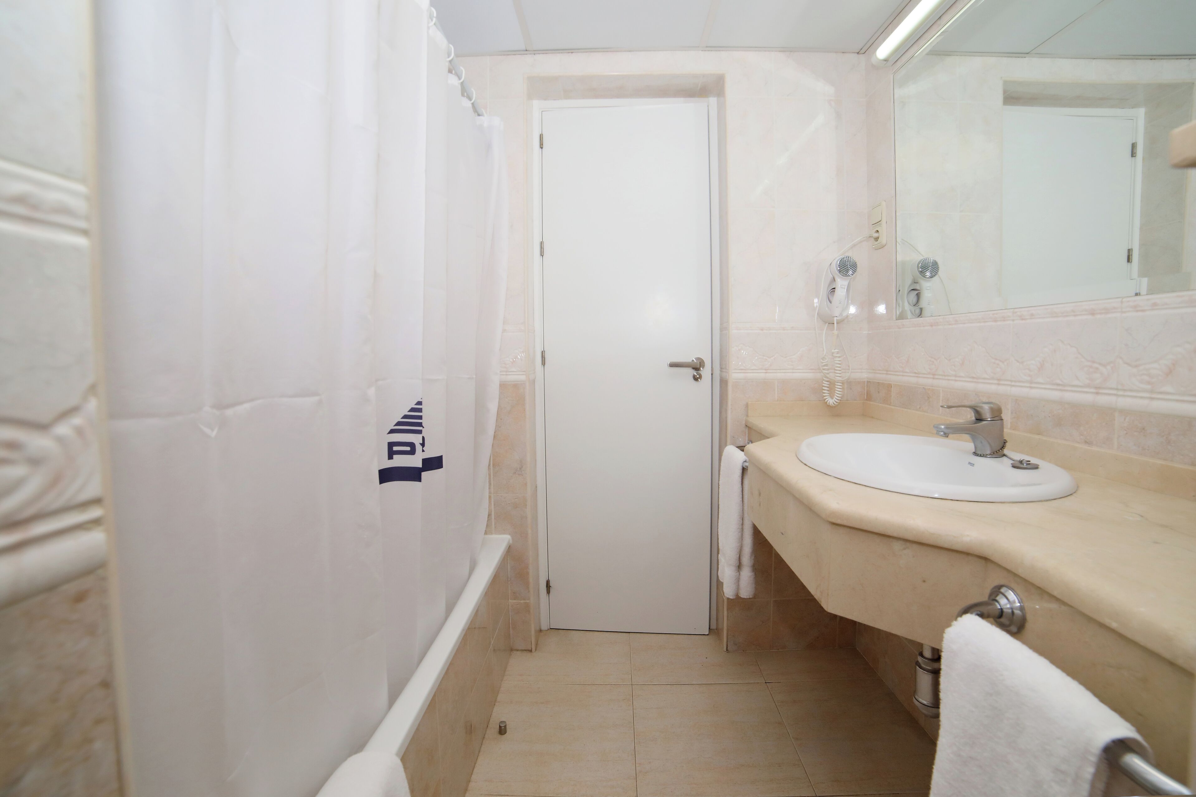 Un baño con puerta blanca, un lavabo, un espejo y un perchero para toallas.
