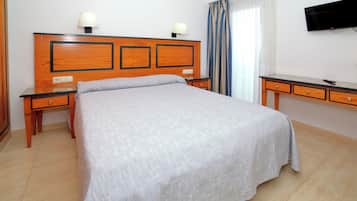 Una habitación de hotel con una cama grande, dos mesitas de noche con lámparas, un televisor de pantalla plana montado en la pared y una ventana con cortinas.