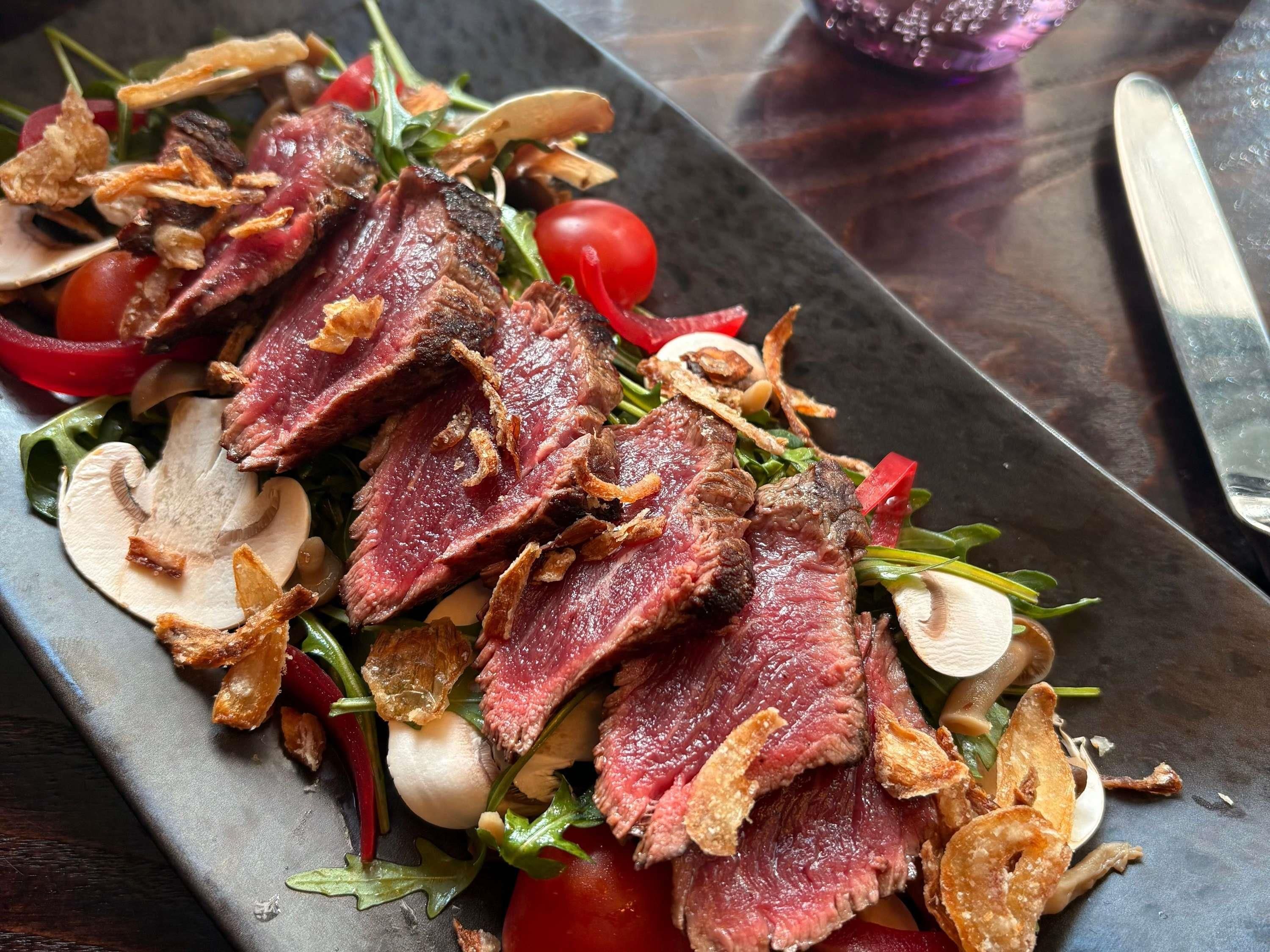 A plate of food with sliced meat, mushrooms, and vegetables.