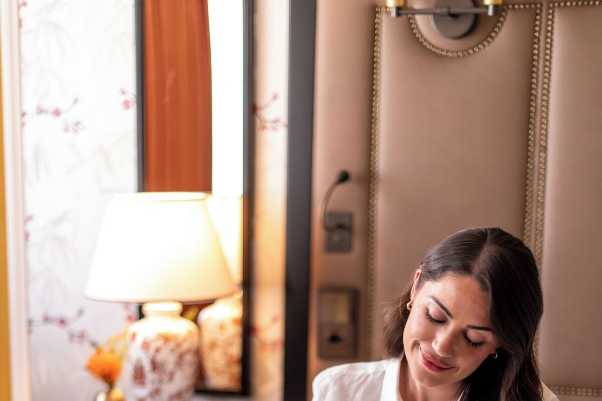 A person sitting on a bed with a tray of breakfast items, including croissants, fruit, and a teapot.