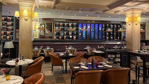Un restaurante con sillas de cuero, mesas dispuestas para comer y una zona de bar con estanterías.