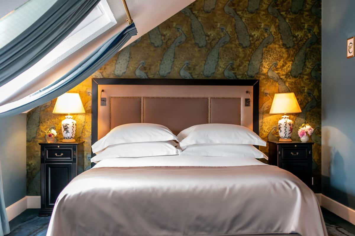 A neatly made bed with white linens, two bedside tables with lamps, and a stone-patterned wall.