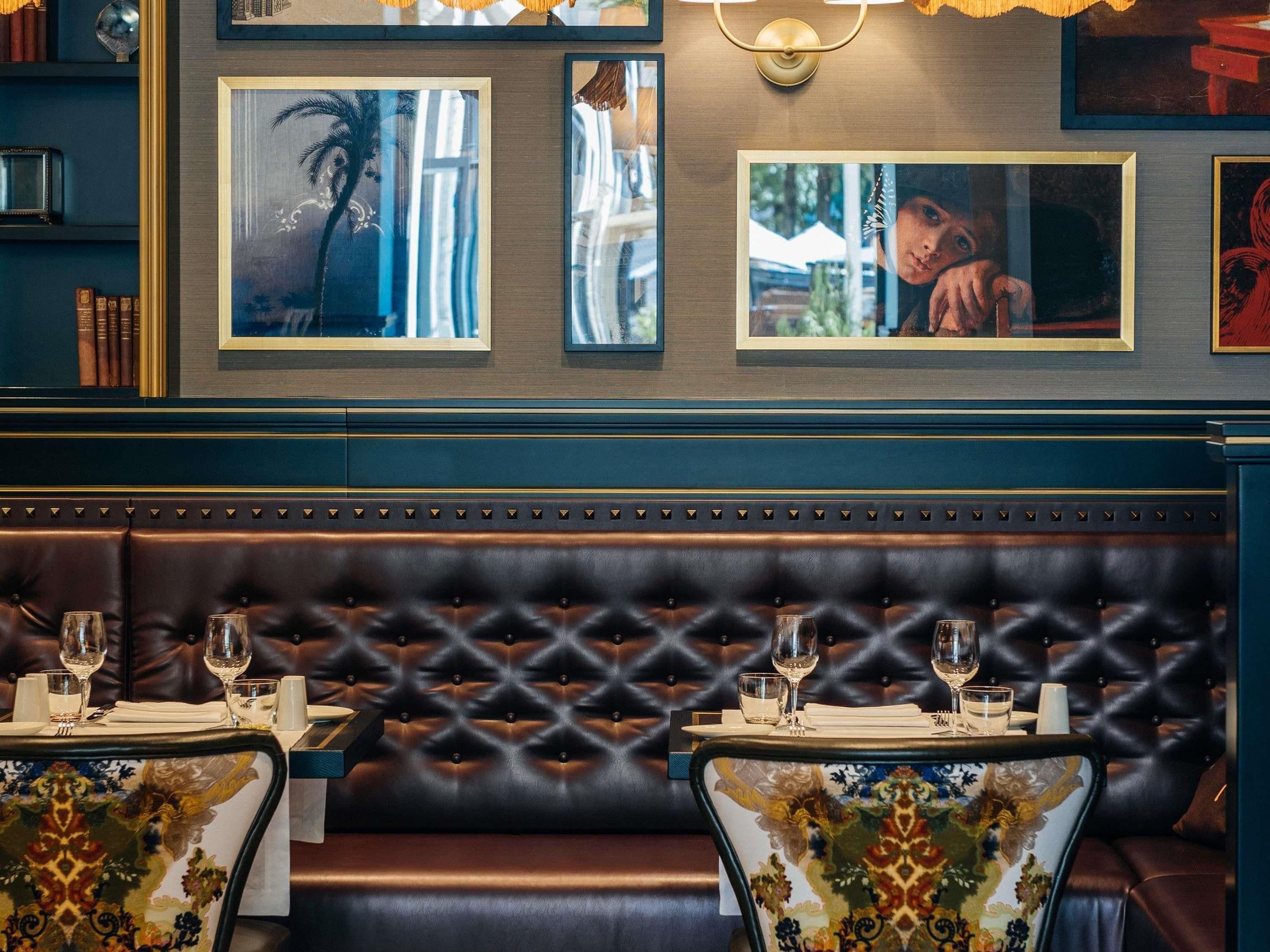 Interior de un restaurante con una zona de asientos en un banco de cuero oscuro, obras de arte en las paredes y una mesa dispuesta con vasos y cubiertos.