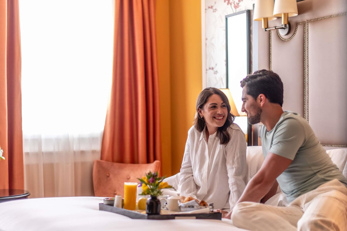 A hotel room with a bed, a tray with breakfast items, and a window with curtains.