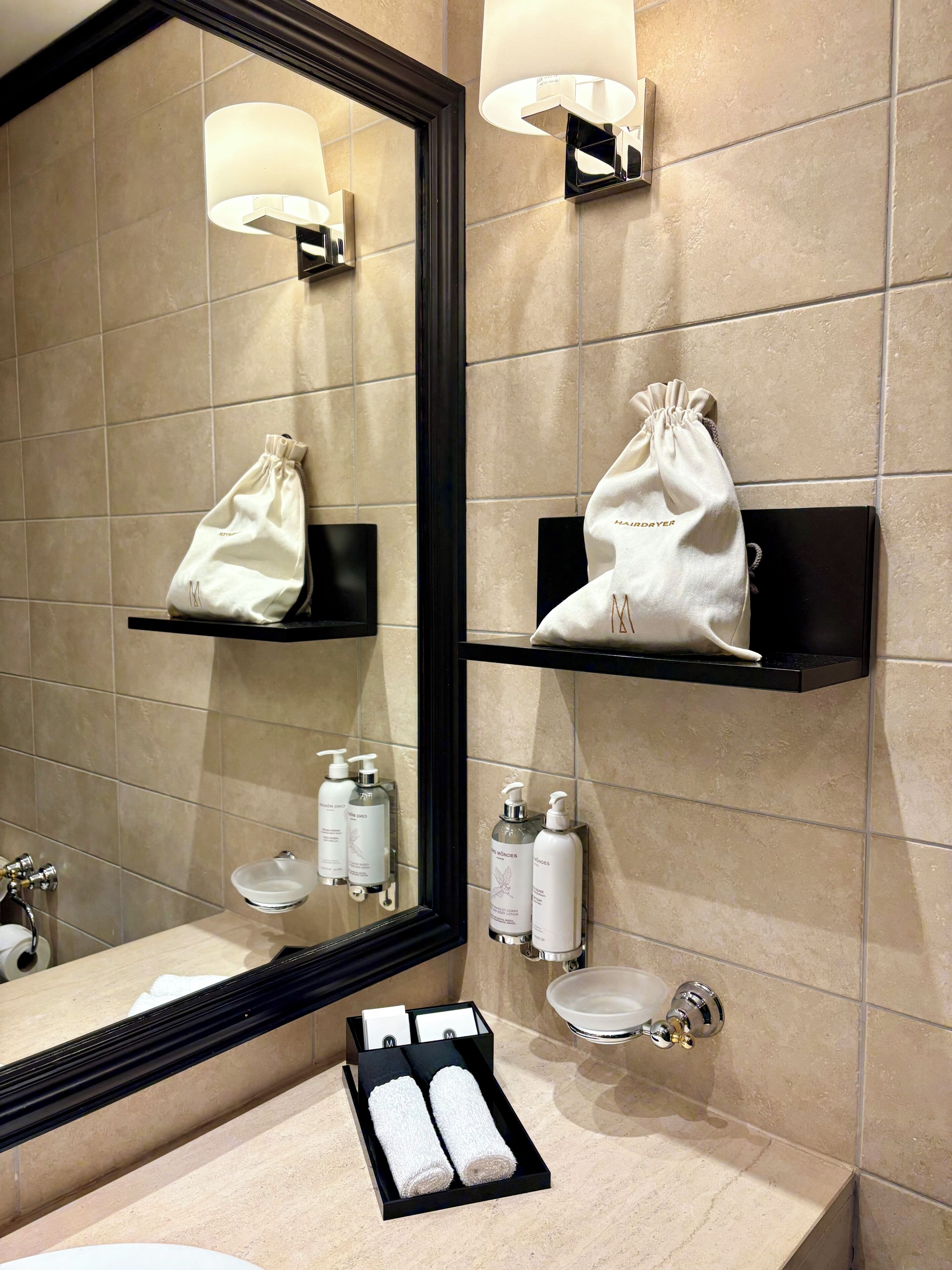 Une salle de bain avec un grand miroir, deux porte-serviettes, un lavabo et des articles de toilette.