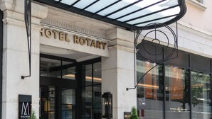 La entrada del Hotel Rotary, con un dosel de vidrio y dos árboles en macetas.