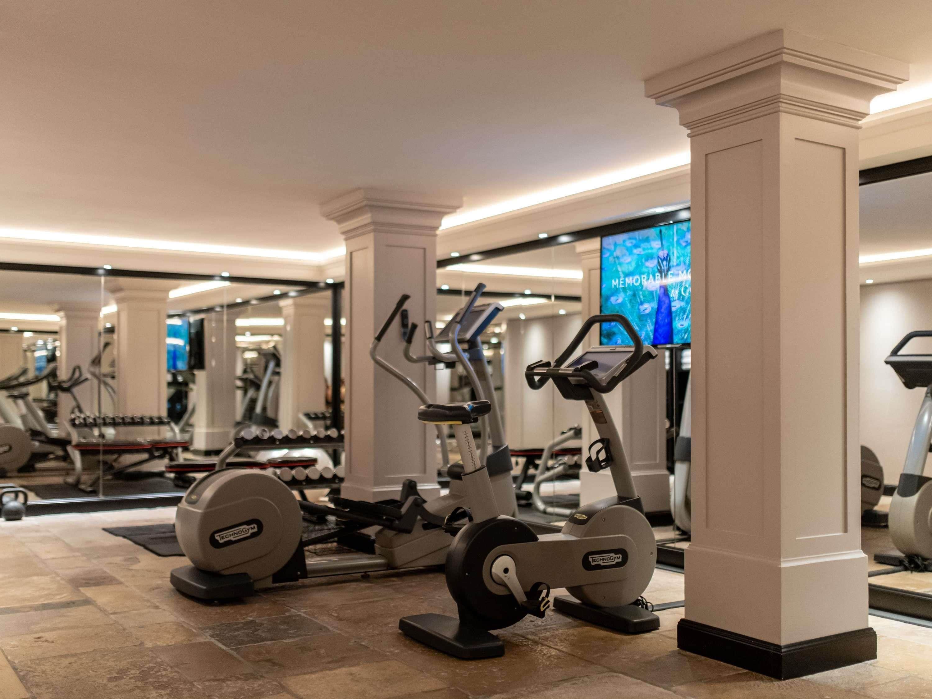 A gym with exercise equipment, a large mirror, and a television screen displaying 'MEMORABLE MOMENTS.'