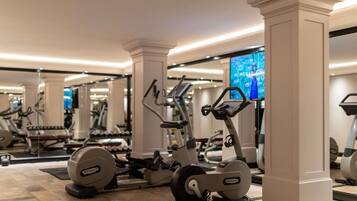 A gym with exercise equipment, a large mirror, and a television screen displaying 'MEMORABLE MOMENTS.'