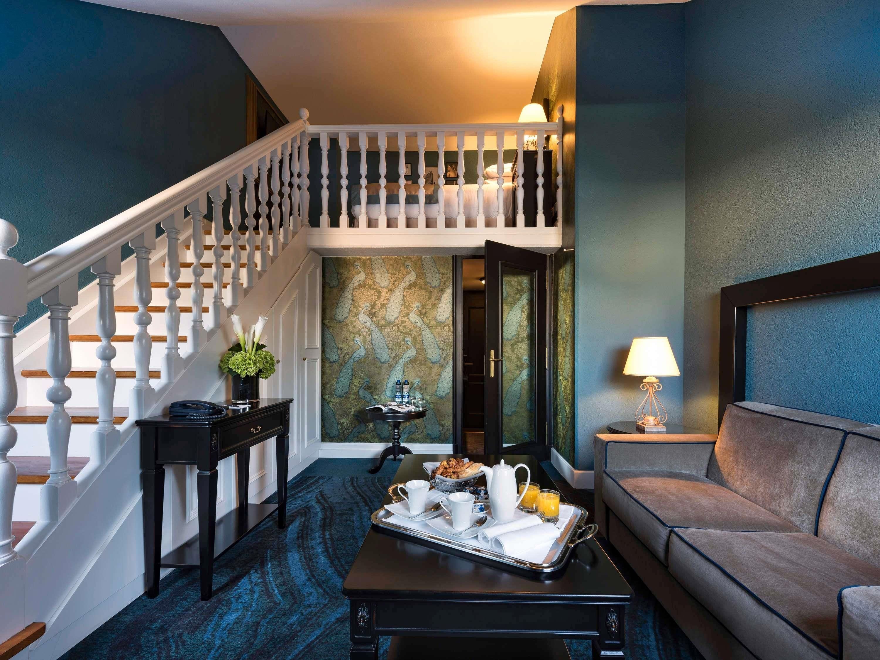 Une chambre d’hôtel avec un escalier, un coin repas où le petit-déjeuner est servi, un canapé et une lampe.