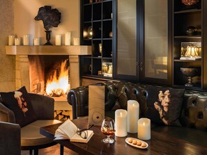 A cozy living room with a fireplace, leather sofas, and a coffee table with a book, glasses, and a glass of wine. - Hotel Rotary Geneva – MGallery (Geneva)