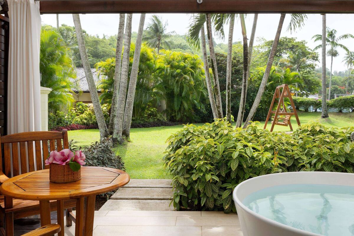 Une terrasse en bois avec une table et des chaises, une baignoire et une vue sur un jardin luxuriant agrémenté de palmiers.