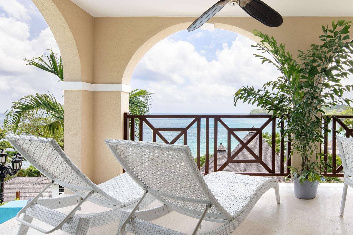 Un balcon avec des fauteuils de jardin en osier blanc, un pot de fleurs et une vue sur la mer.