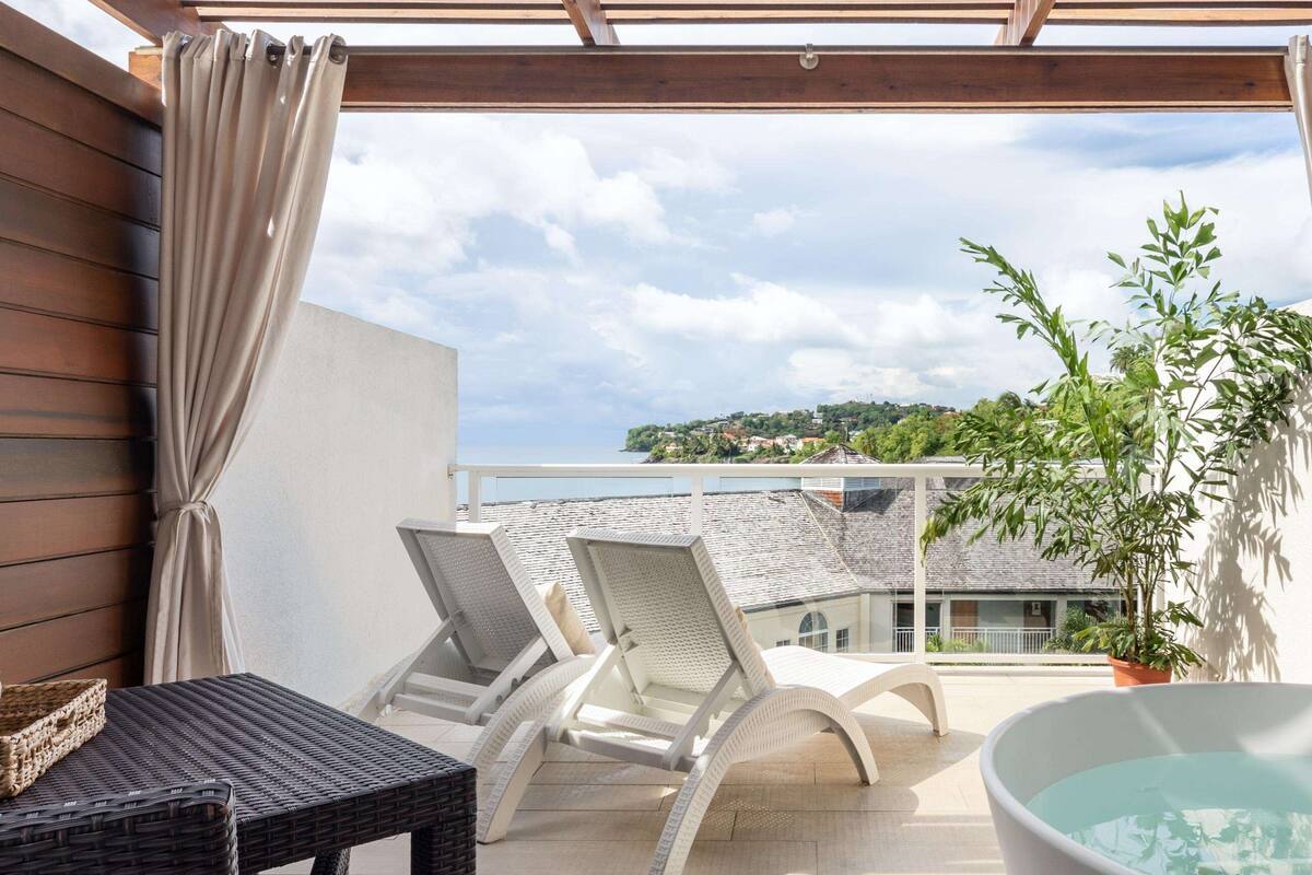Un balcon avec deux fauteuils, une petite table, une plante en pot et une baignoire.
