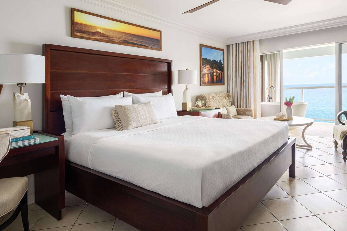 Une chambre d’hôtel avec un grand lit, un bureau, une chaise, une petite table et une vue sur la mer.
