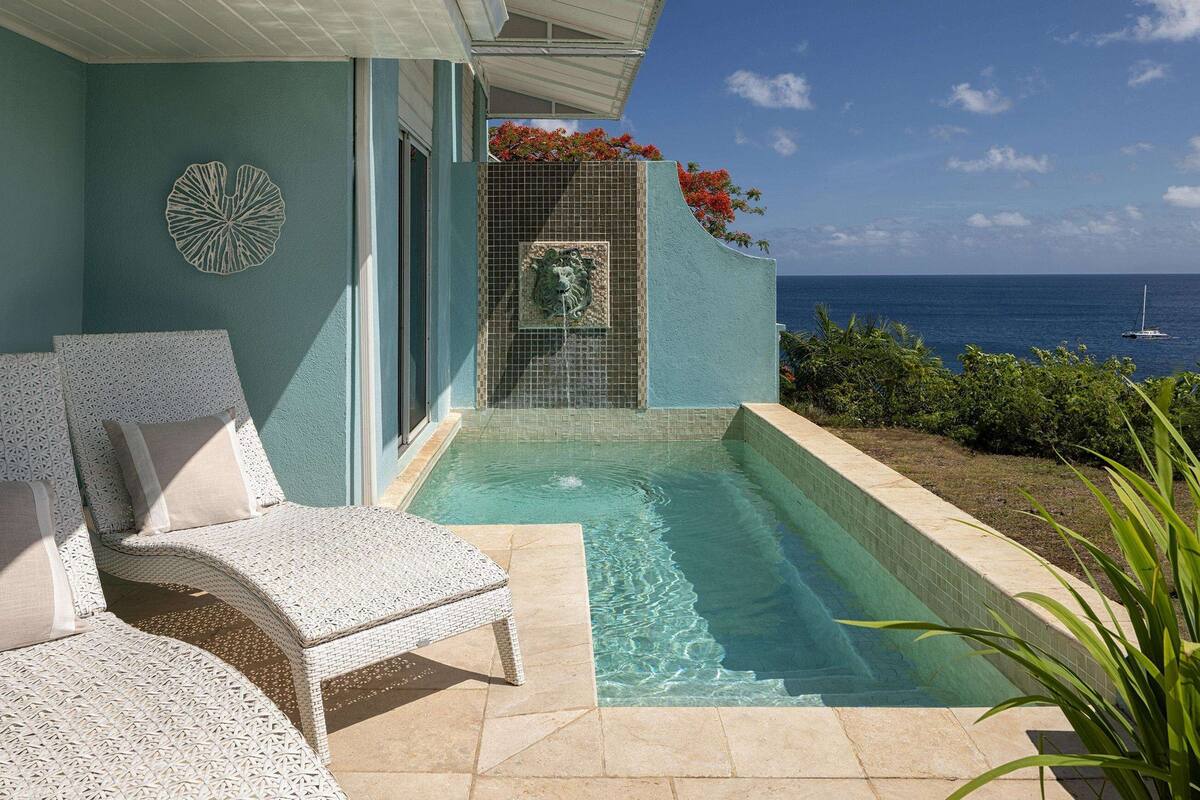 Un espace piscine avec vue sur l’océan, un mur décoratif et des sièges d’extérieur.
