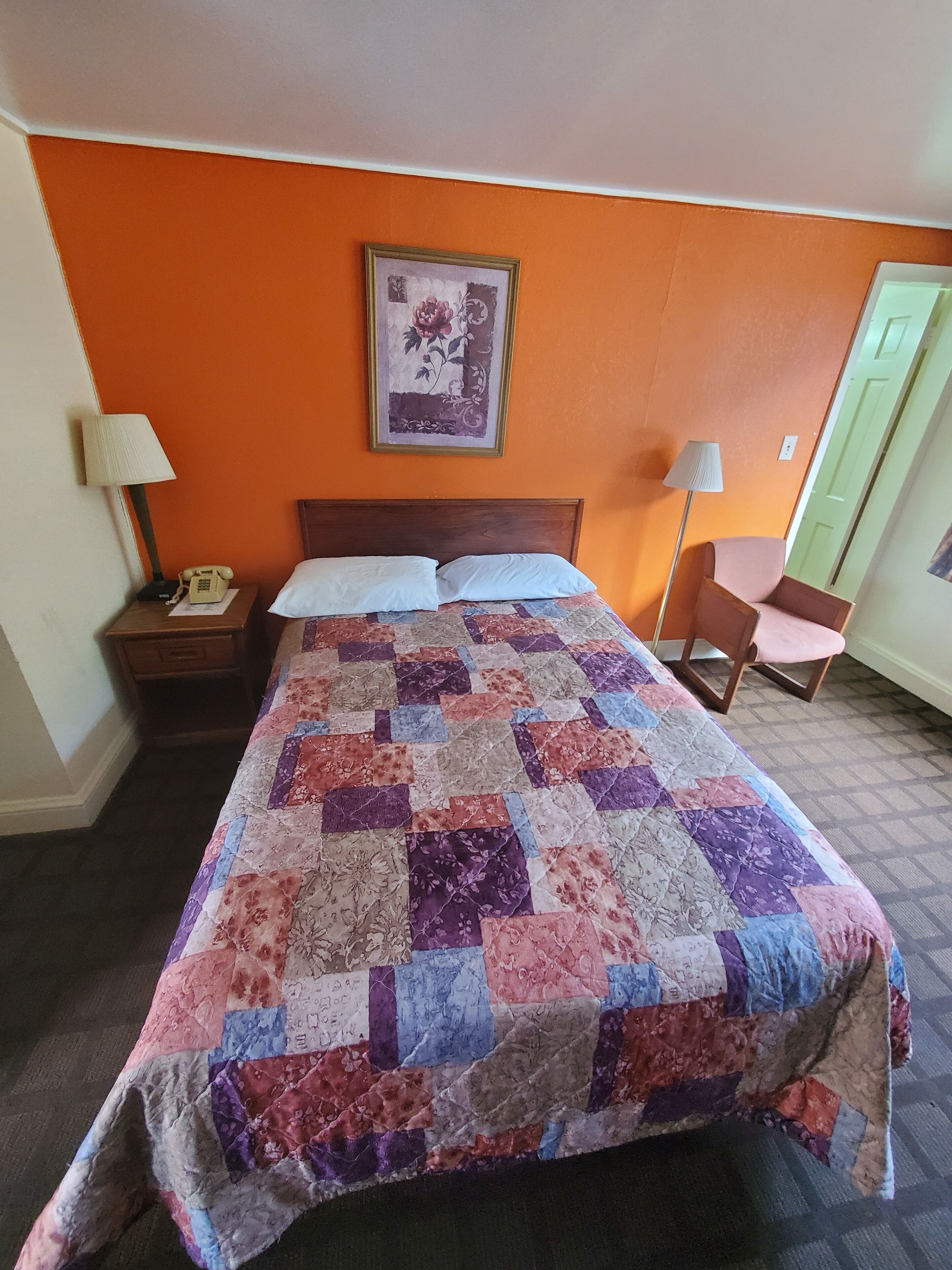 Una habitación de hotel con una cama grande, una mesita de noche con lámpara, una silla y una puerta.