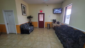 A waiting area with two sofas, a coffee table, a trash bin, a door labeled "Restroom", and a TV mounted on the wall.