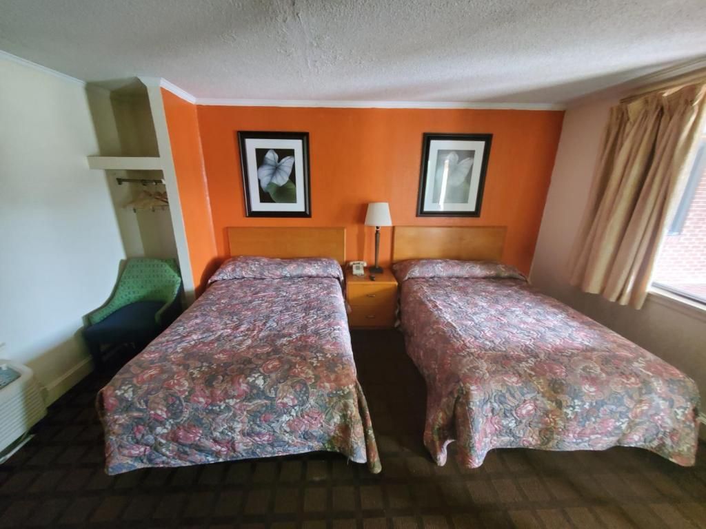 A hotel room with two single beds, a nightstand, a lamp, and a window with curtains.