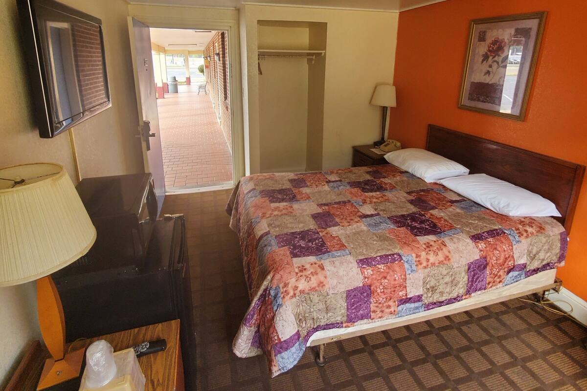 A hotel room with a bed, a desk with a lamp, a television, and a painting on the wall.
