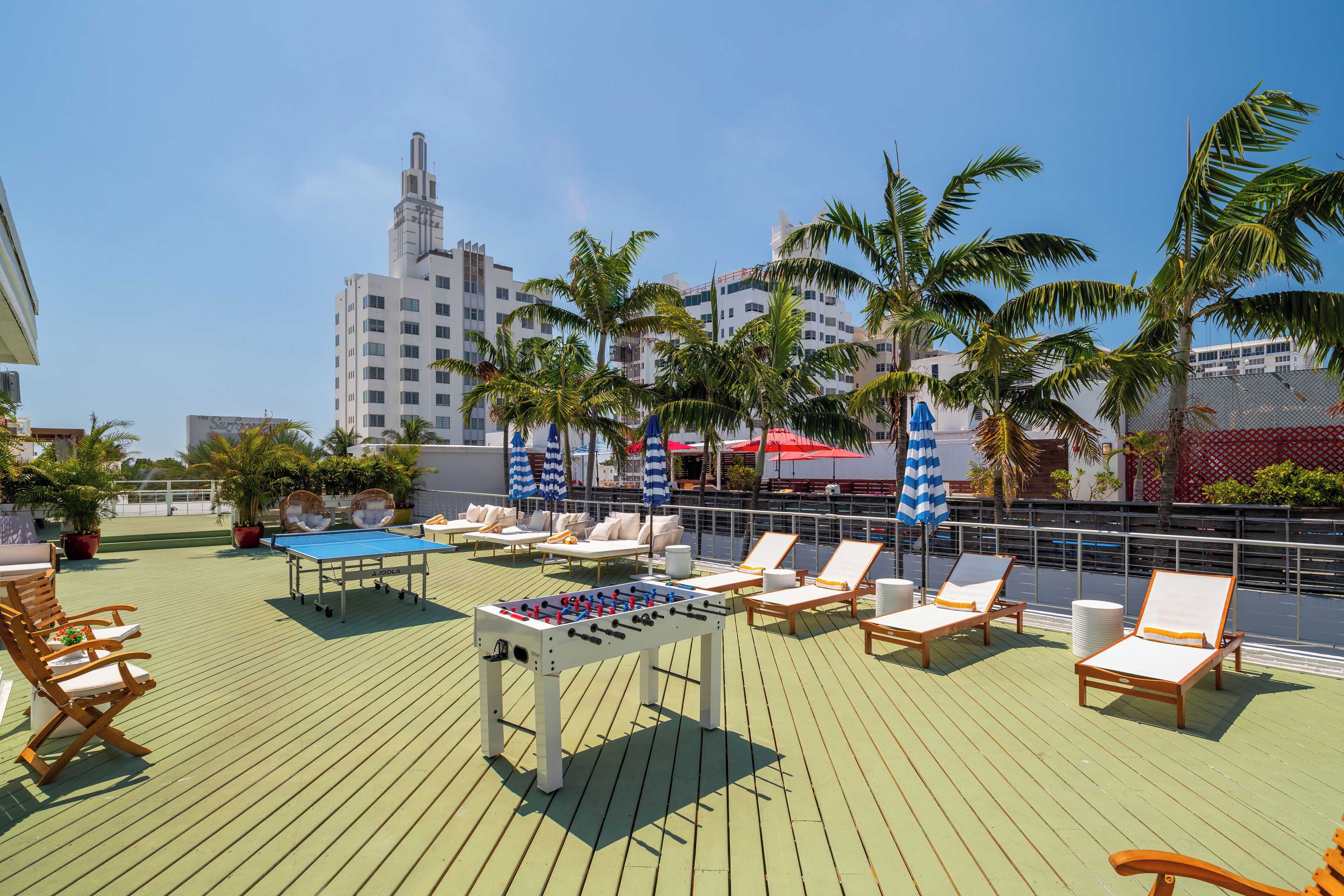A rooftop deck with a foosball table, lounge chairs, and palm trees.