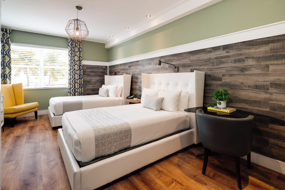 Une chambre moderne avec deux lits, une chaise jaune, une petite table avec une plante et un luminaire au design géométrique.