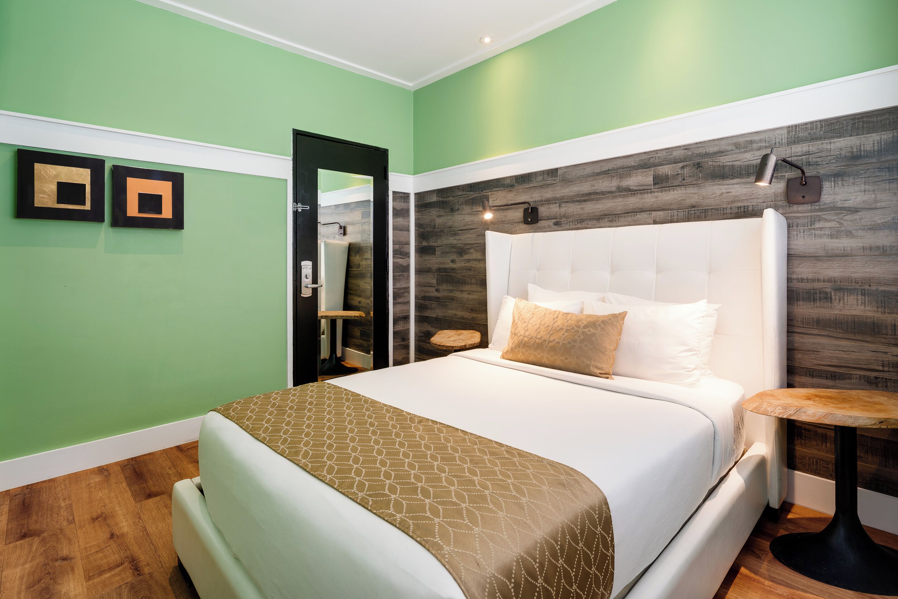 Un dormitorio con una cama grande, un cabecero de madera, una mesita de noche y una pared verde con dos cuadros enmarcados.