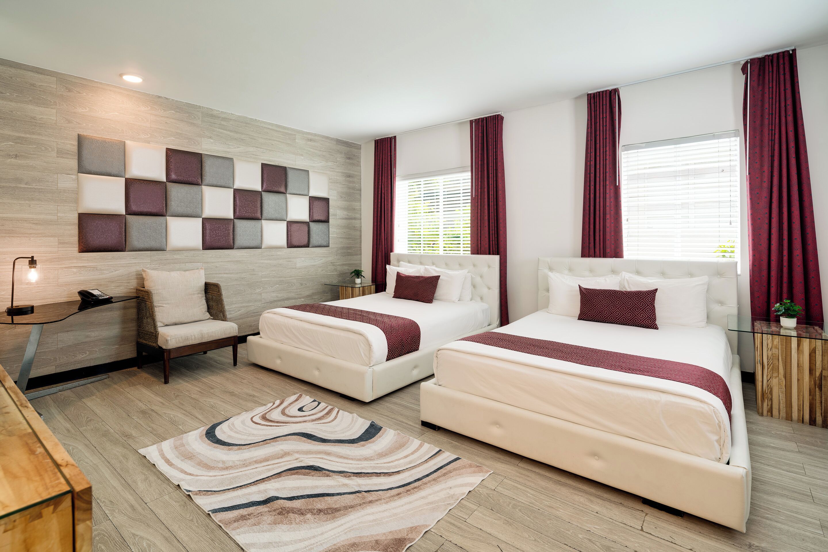 A modern bedroom with two beds, a wall-mounted light fixture, a bedside table, and a large window with curtains.