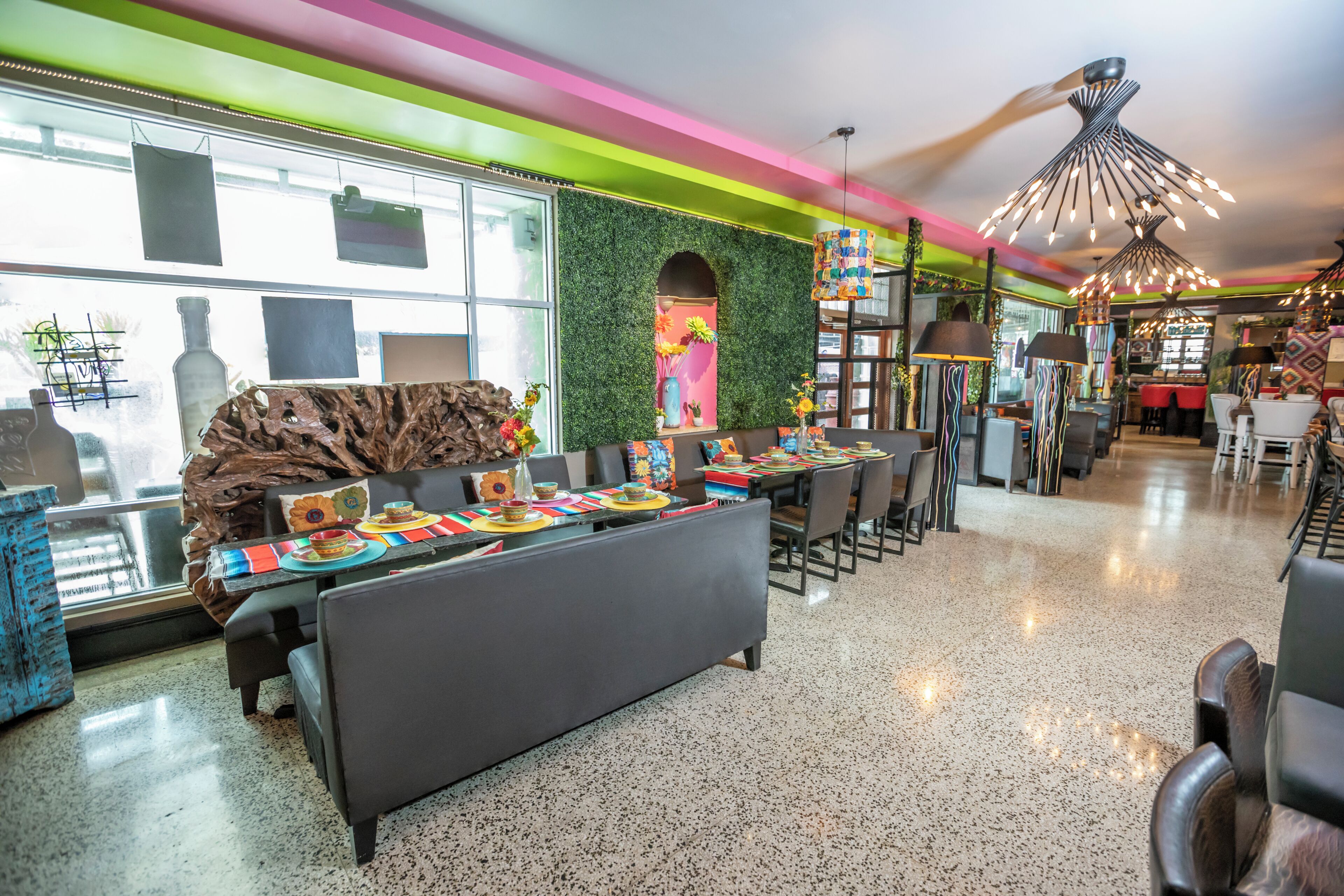 A modern restaurant with a long communal dining table, black upholstered seating, and colorful table settings.