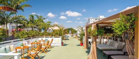 A rooftop deck with wooden lounge chairs and a pool.