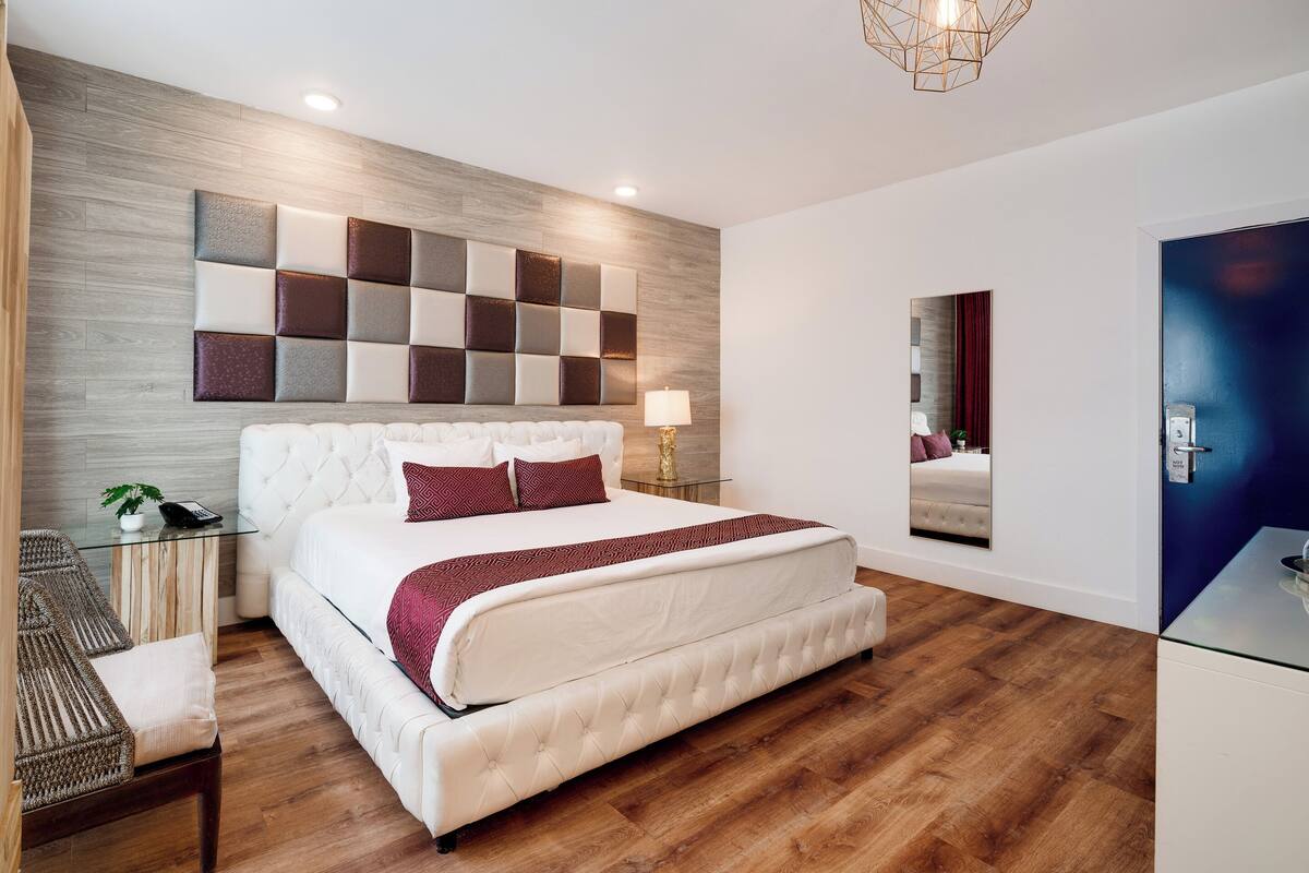 Une chambre à coucher moderne avec un grand lit, une tête de lit en bois, un miroir et une table de chevet avec une lampe.