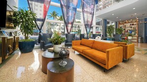 Un hall d’entrée moderne avec un grand canapé orange, des fauteuils noirs, un globe terrestre posé sur une table et une grande plante en pot.